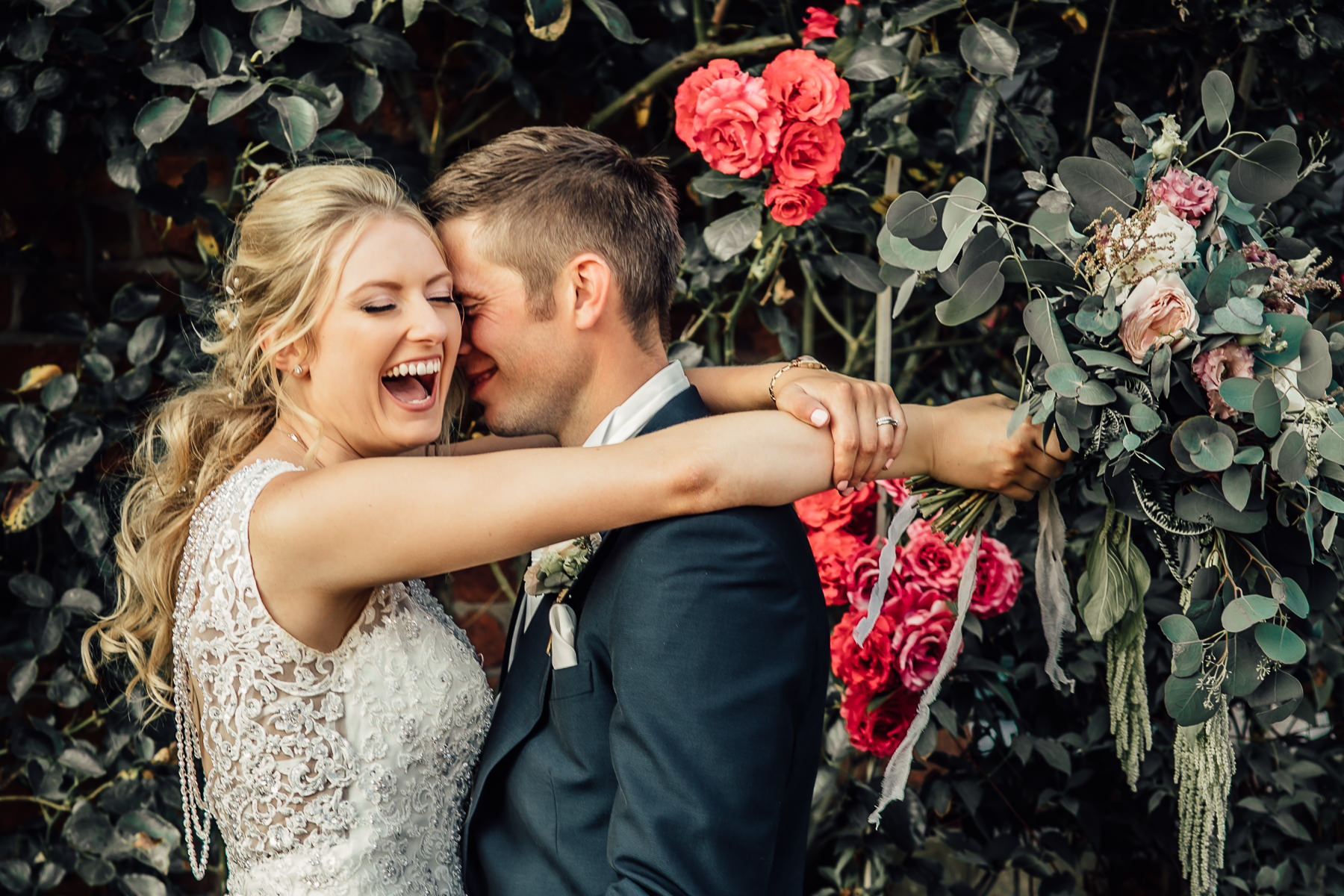 Bride laughing while hugging her husband and holding her flowers