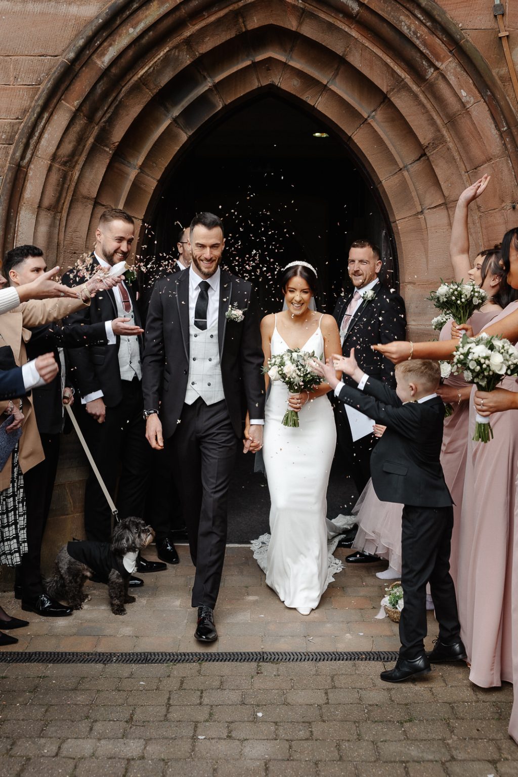a group of people standing in front of a stone archway throwing confetti on the bride and groom