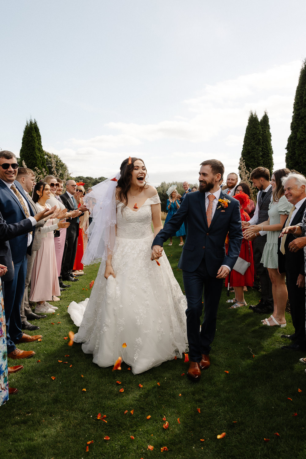 a bride and groom walking down a lawn with people in the background